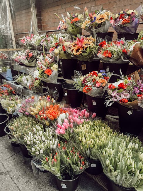 A diverse display of fresh floral bouquets arranged in black buckets on a shop floor, showcasing an array of flowers including tulips in shades of pink, white, and red, as well as mixed arrangements o